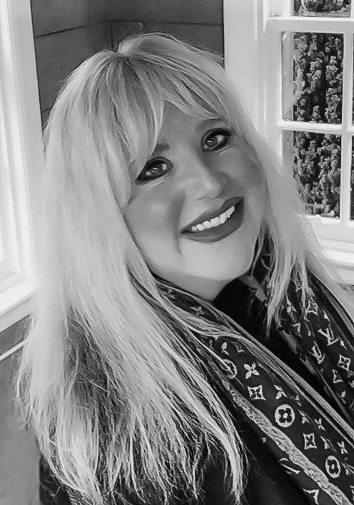 Black and white portrait photo showing a bright smile and platinum blonde hair, wearing a Louis Vuitton scarf.