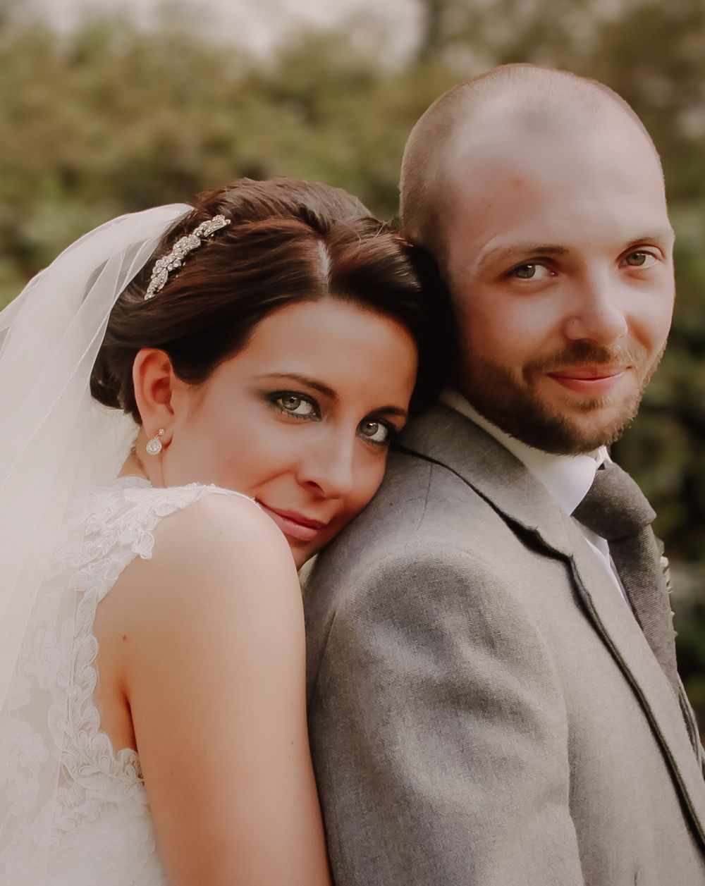 A couple poses together on their wedding day in an intimate portrait with warm natural lighting and blurred outdoor background.