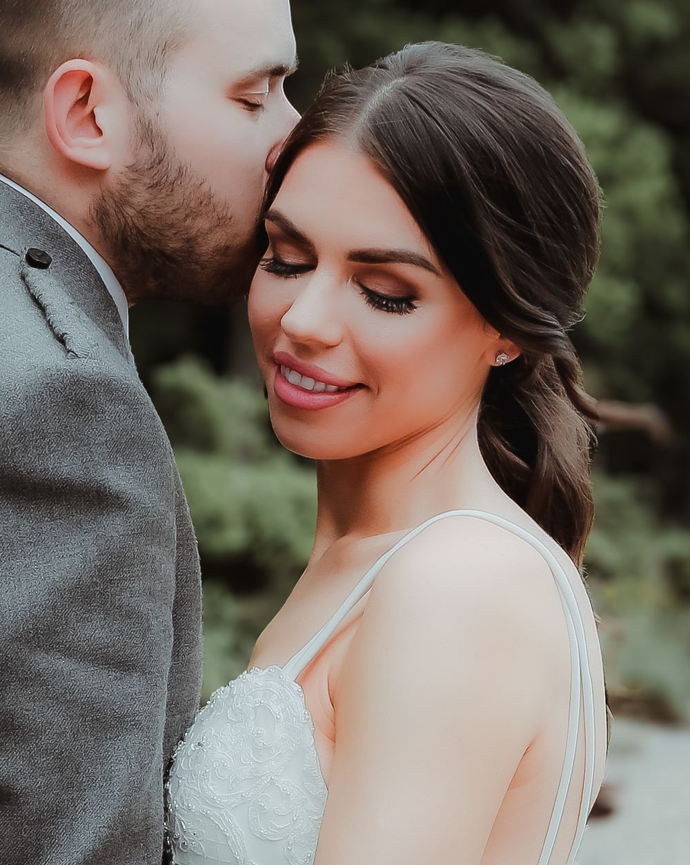 Romantic wedding portrait showing tender intimate moment between newlyweds outdoors with natural greenery in background.