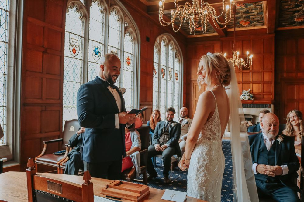 Two people exchanging vows during a wedding ceremony inside a beautiful Gothic-style room with stained glass windows.