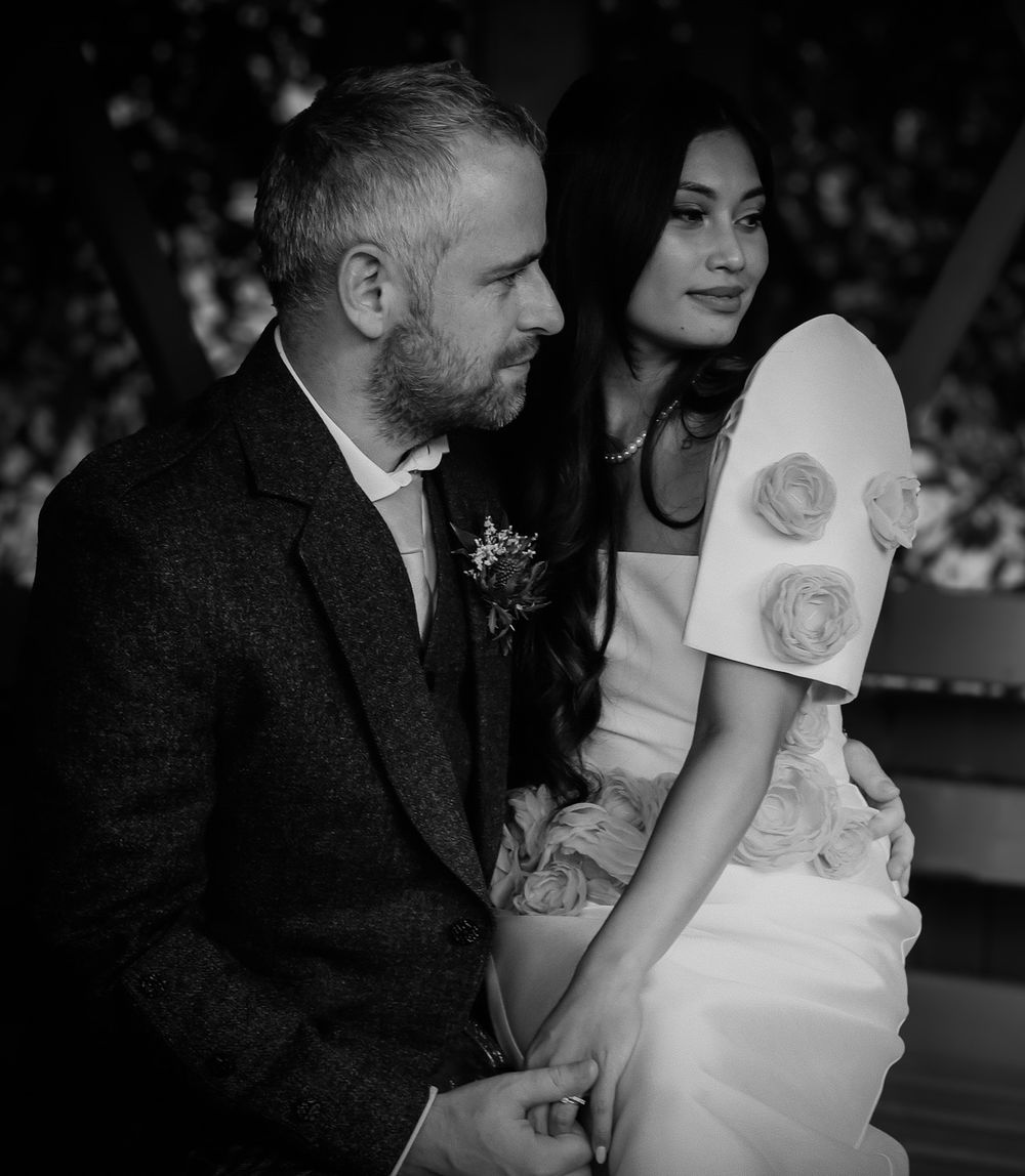 A romantic black and white wedding portrait showing a couple in an outdoor garden setting.